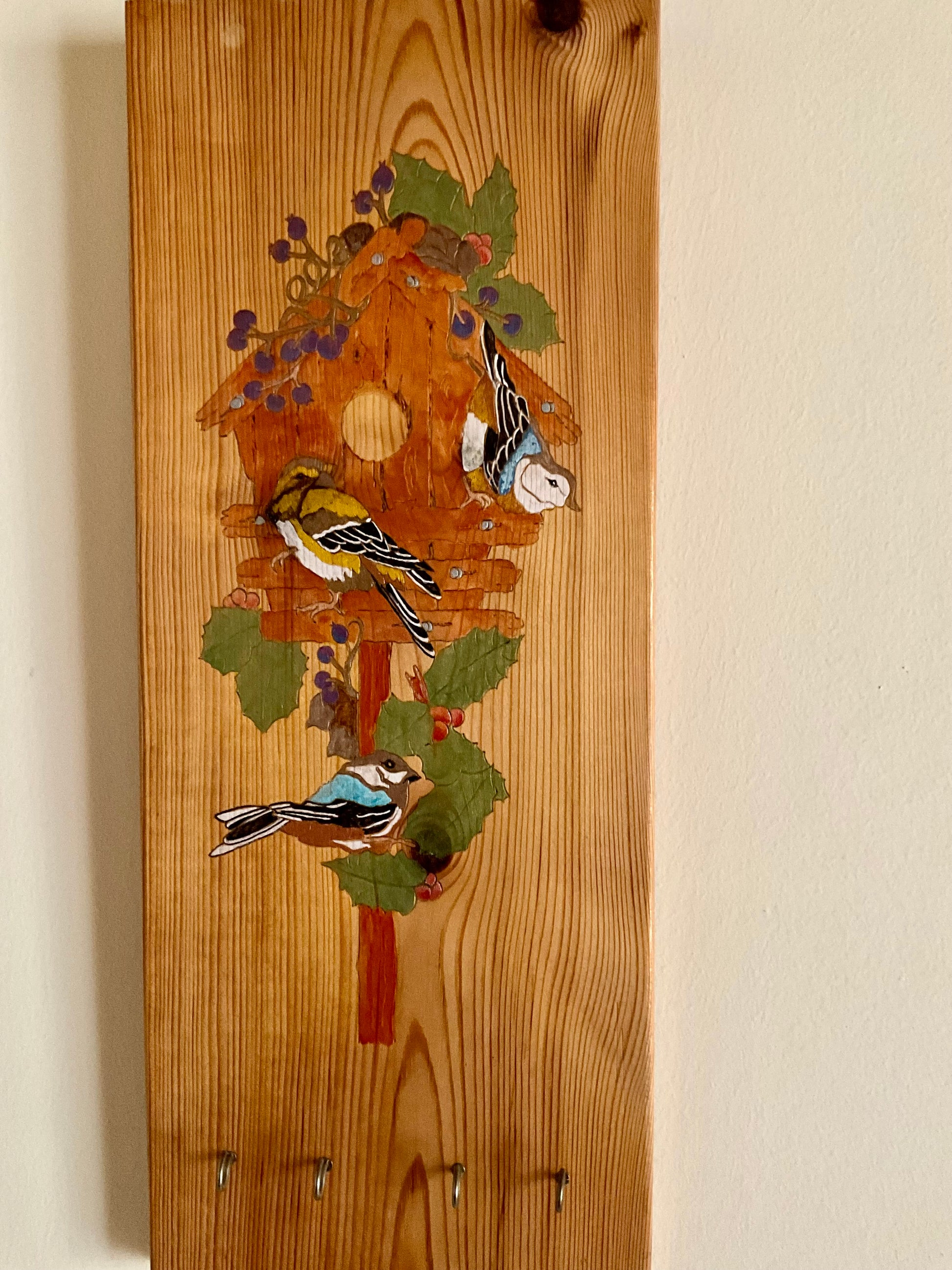Organize your home and add a touch of nature with Home to Roost, a wall-mounted wooden key holder featuring a hand-painted design of colourful song birds perched outside a bird box. Keep your keys in one place and bring a charming, original artwork into your space. 8” x 19”