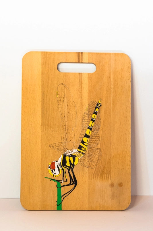 A beach wood chopping board, wood-burnt with design of a dragonfly landing on a stalk. Finished with acrylics.