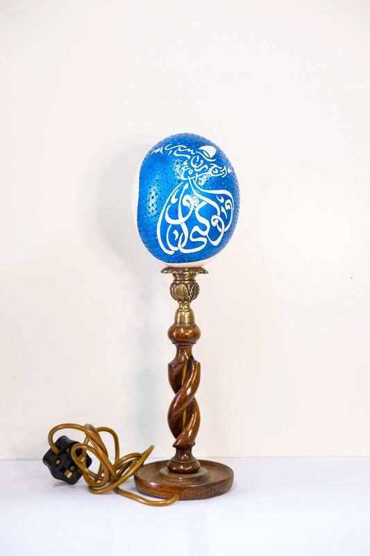 Carved and painted ostrich egg lamp depicting a whirling dervish dancer. Set upon a carved wooden and brass holder. Mains powered. 40cm tall.