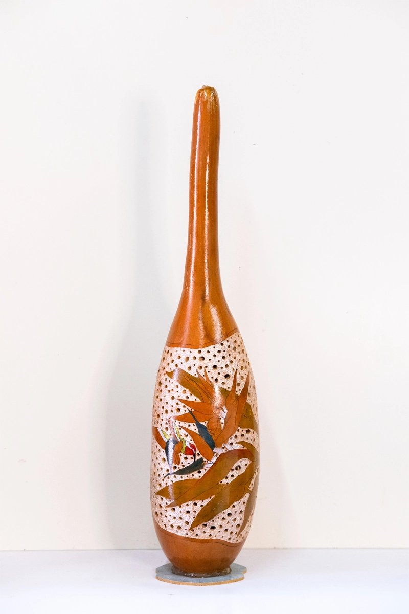 A gourd lamp depicting a hummingbird taking nectar from a bird of paradise flower. Wood-burnt carved and finished with wellburn inks. Battery powered. 52cm tall.