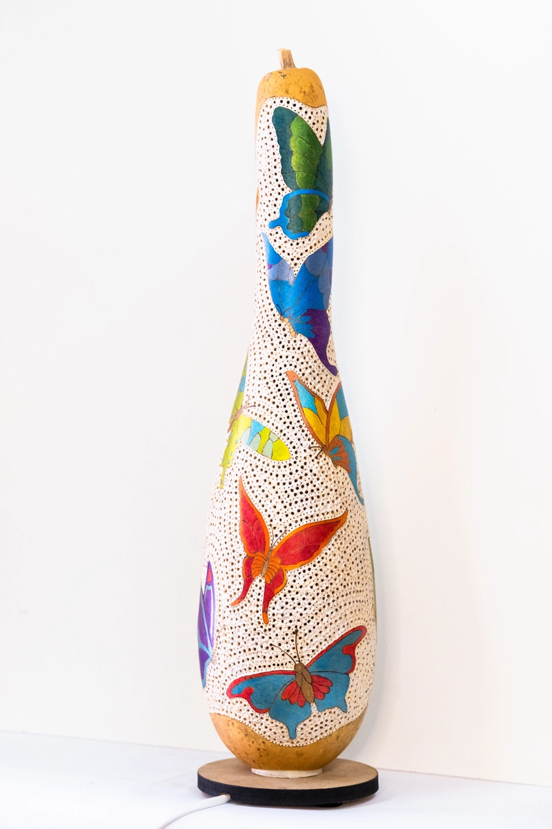 'A tall bodied gourd lamp, depicting different types and coloured butterflies . Wood-burnt, carved and finished in acrylic. Mains powered. 54cm tall.