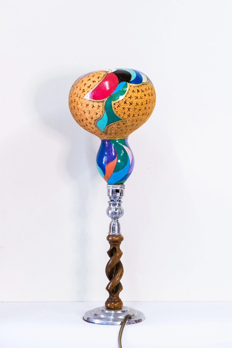 An upside down bottle gourd with beautifully designed patterns that’s mounted onto hardwood and silver coloured base. Wood-burnt, carved and finished in acrylics. Mains powered. 44cm tall