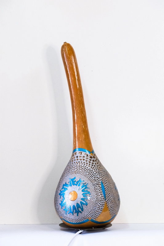 A gourd lamp with a delicately carved decreasing circular effect on three sides. Wood-burnt, carved and finished in acrylics on a circular metal base. Mains powered. 56cm tall