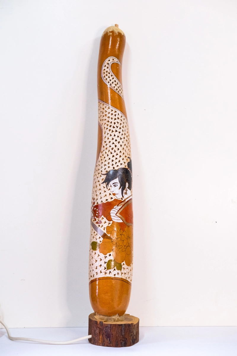 A tall gourd lamp depicting a female Japanese warrior on a wooden base. Wood-burnt, carved and finished in wellburn inks. Mains powered. 70cm tall