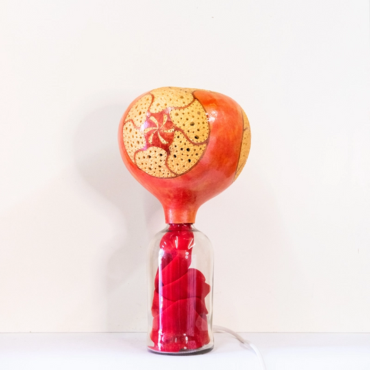 A gourd lamp designed by carving on three sides and mounted on a glass bottle and finished in wellburn inks.mains powered. 37cm tall.