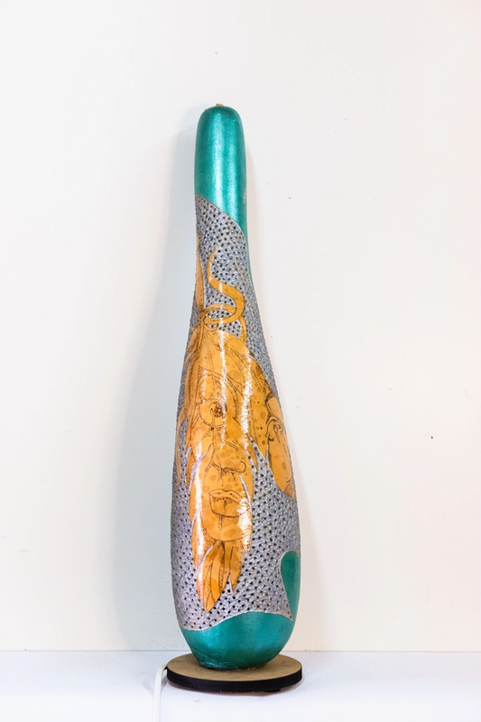 Gourd lamp wood-burnt and carved to form a face on a feather, finished with acrylics on a wooden base. Mains powered. 58cm tall