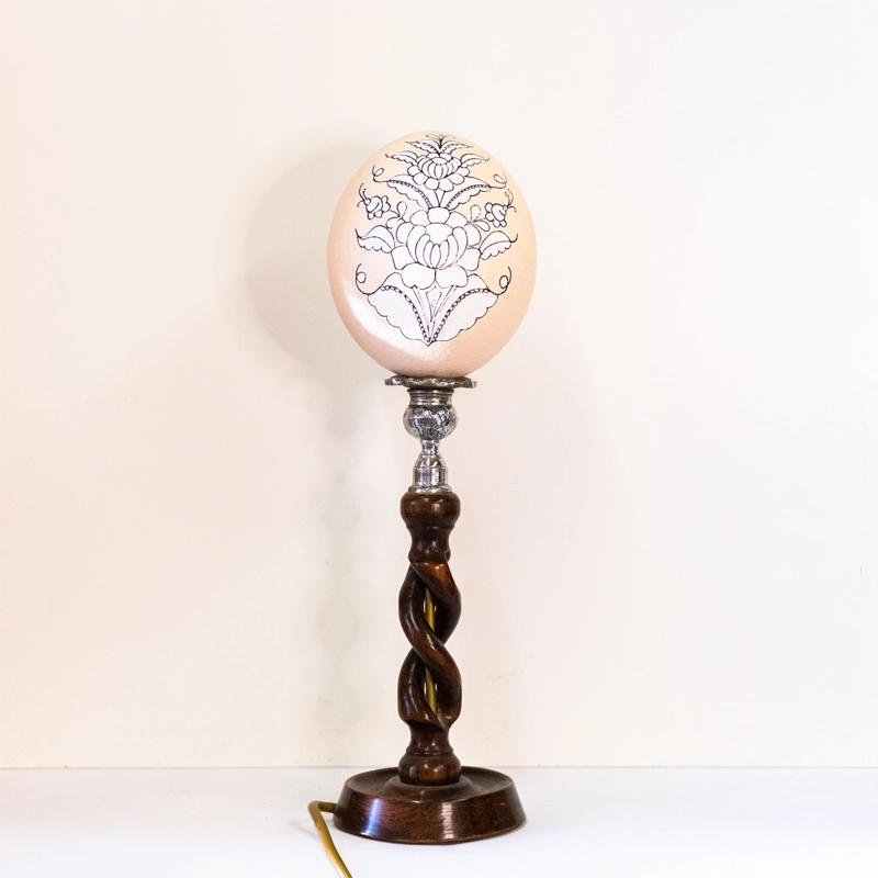 Ostrich egg carved and mounted on a metal and wooden base. Mains powered. 40cm tall.